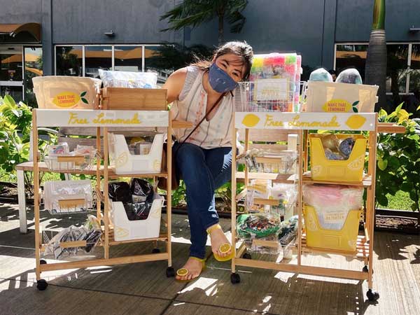 Seated woman wearing face mask posing next to carts with fund-raising food items